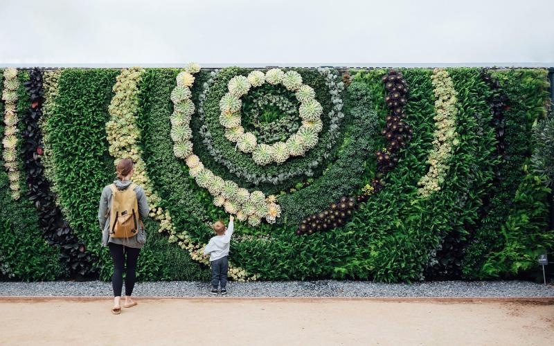 mother and child standing in front of a mural made of plants